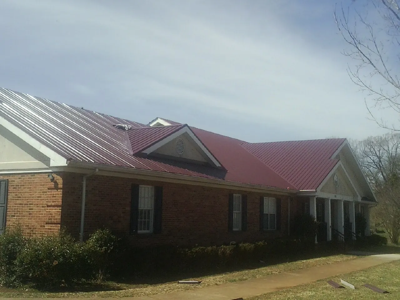 Red metal roof with gabled entries on a long brick building, from a Hail Damage Roof Repair job in Morgan